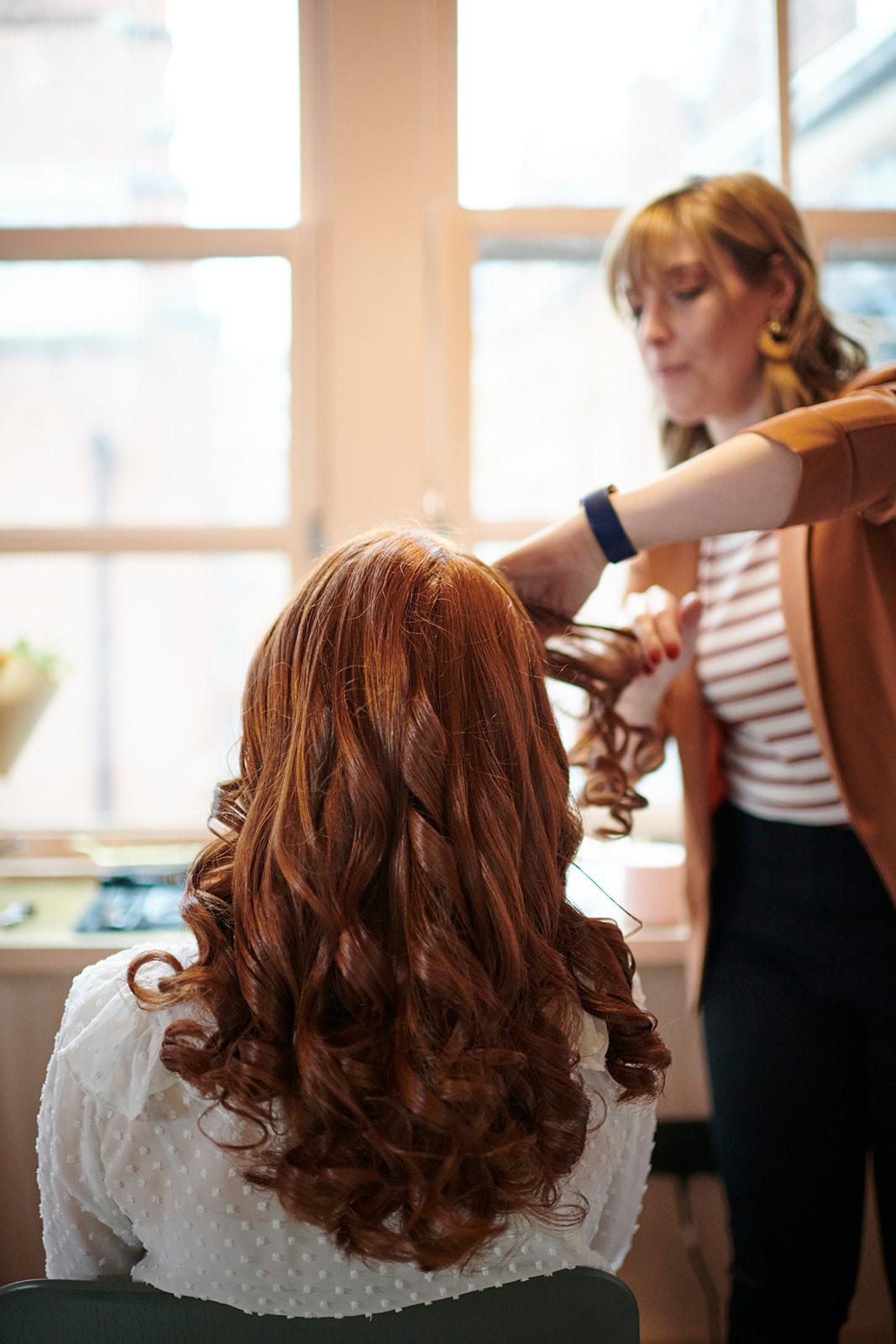 This is a photo of a wedding and events hairstylist prepping the hair for a client ahead of the wedding day. It is a trial preview appointment with a bride to be and her hairstylist chatting and discussing hair options for the wedding day